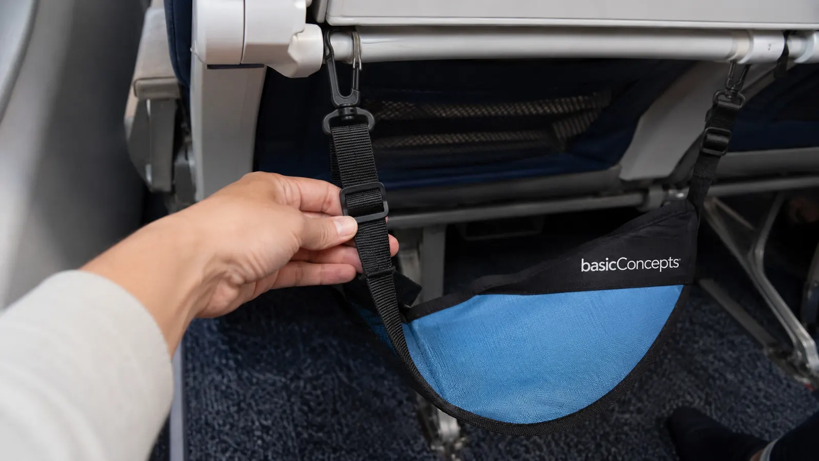 Hand adjusting the strap of the BASIC CONCEPTS foot hammock under an airplane tray table