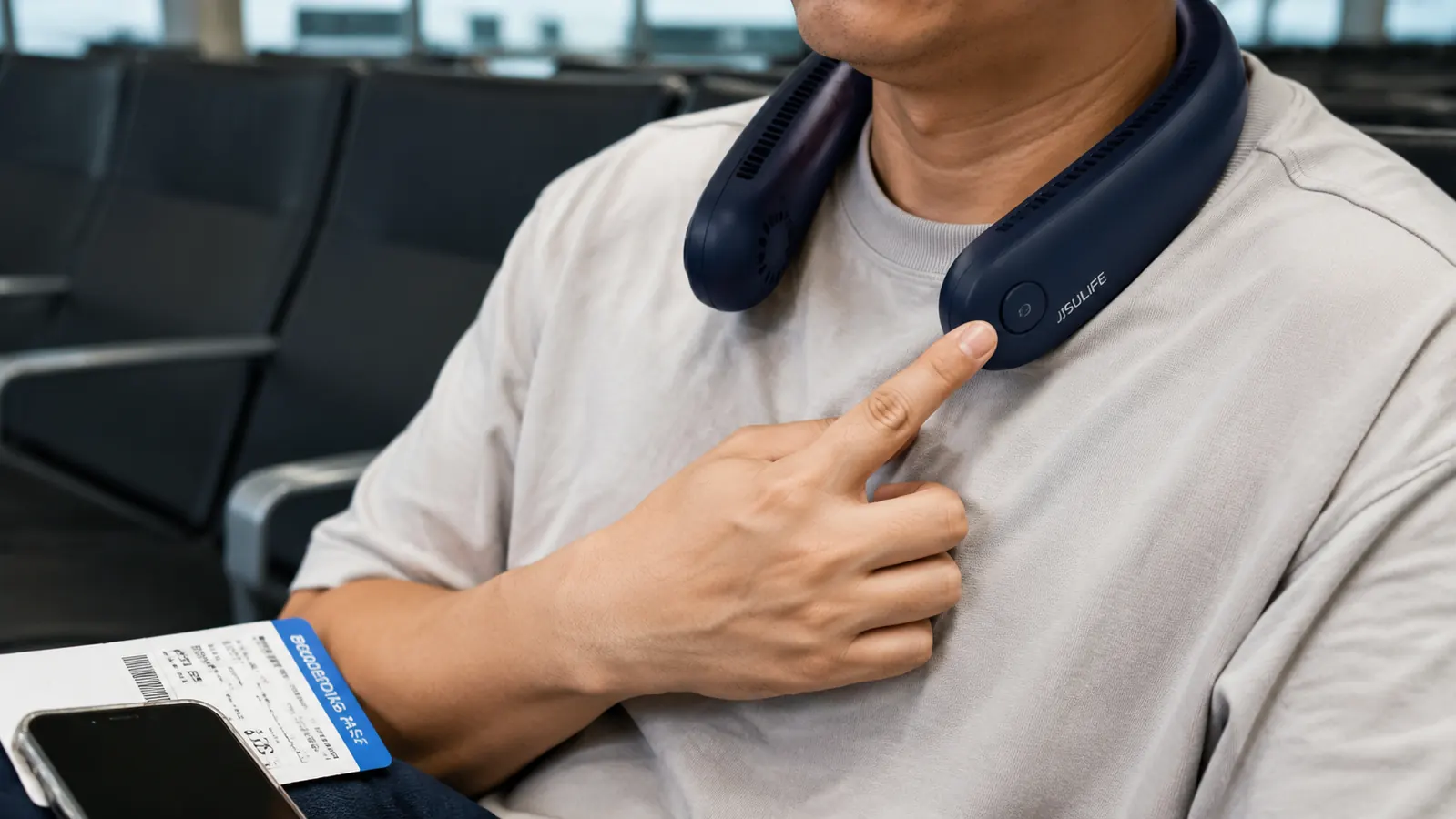 Hand adjusting the speed button on a black bladeless neck fan while seated at a gate